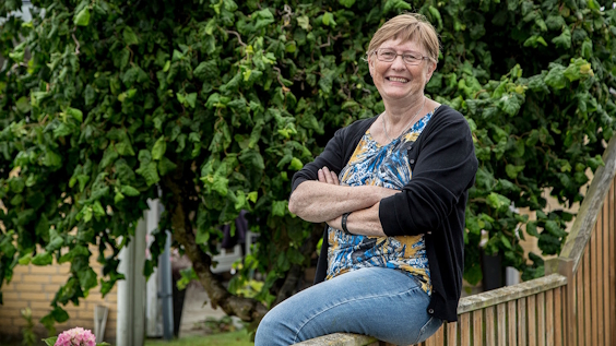 Smilende kvinde sidder på plankeværk i have